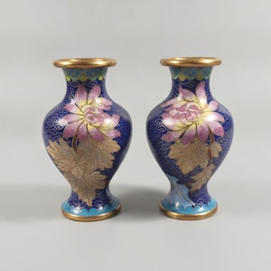 May include: A pair of matching cloisonné vases featuring a deep blue background with intricate gold wire patterns. Each vase displays a prominent pink and yellow flower with gold-toned leaves, finished with a gold rim and base.