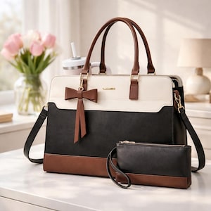 May include: A tri-color handbag with a matching wallet. The handbag features a white top, black center, and brown base. It has brown handles and a brown bow-shaped charm. The wallet is black with a brown base and a wrist strap.