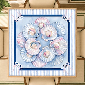 Puede incluir: Un mantel cuadrado con una ilustración central en acuarela de varias conchas de vieira blancas y rosas, cada una con una perla. El borde tiene un patrón de rayas azules y blancas con pequeños lazos blancos en cada una de las cuatro esquinas.