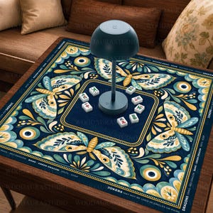 Può includere: Un tappetino da mahjong quadrato con sfondo blu scuro e un motivo ripetuto di falene color crema e verde acqua, dettagli dorati e motivi circolari. Una lampada verde scuro a forma di fungo si trova al centro con sei tessere bianche.