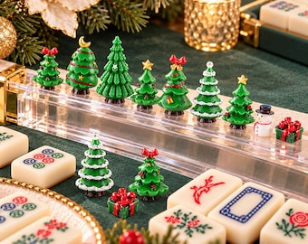 Puede incluir: Una colección de árboles de Navidad en miniatura de resina, un muñeco de nieve y cajas de regalo dispuestas sobre un soporte de acrílico transparente, junto a varias fichas de mahjong con motivos florales y geométricos.