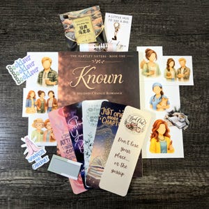 Könnte beinhalten: Eine Sammlung von Artikeln zum Thema Bücher, darunter ein Buch mit dem Titel "Known", Lesezeichen, Aufkleber und Tee. Die Lesezeichen enthalten Zitate wie "Don't lose your place... or the gossip." und "Just one more chapter".