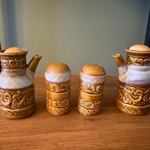 Könnte beinhalten: Ein Vintage-Salz- und Pfeffer-Set aus Keramik mit zwei kleinen Teekannen und zwei Streuern. Das Set ist hauptsächlich braun mit cremefarbenen und goldenen Akzenten. Die Teekannen haben Griffe und Ausgüsse, die Streuer sind zylindrisch.