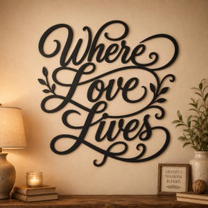 Könnte beinhalten: Ein Wandkunstobjekt aus schwarzem Metall mit dem in Schreibschrift gehaltenen Text Where Love Lives, verziert mit dekorativen Schnörkeln und Blattmotiven. Das Design besteht aus miteinander verbundenen Buchstaben und Linien.
