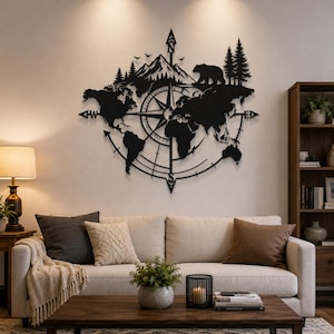 May include: A black metal wall art piece featuring a world map silhouette integrated with a compass rose design. The top section displays a mountain range, pine trees, and a bear silhouette. The compass points are marked with N, S, E, and W.