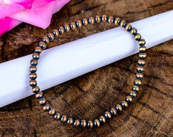 May include: A circular bracelet composed of small, uniform spherical beads with a metallic finish. The beads feature a dual-tone appearance, blending dark charcoal grey tones with warm copper highlights along their rounded surfaces.