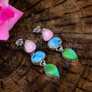 May include: A pair of dangle earrings featuring three stones each in a vertical arrangement. The stones include a smooth pink heart-shaped cabochon, a round blue turquoise-style stone with brown matrix, and a pear-shaped green stone, all set in silver.