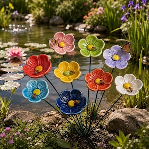 May include: A collection of nine ceramic flowers on thin metal stems, each featuring five rounded petals in various colors including pink, green, purple, red, yellow, blue, orange, and white, with yellow centers and small bees resting on them.