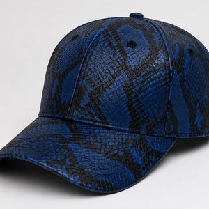 Pode incluir: Um boné de beisebol com um padrão vibrante de pele de cobra em azul e preto. O boné tem uma coroa estruturada de seis painéis, uma aba curva e um pequeno botão no topo central. O material texturizado cobre todo o exterior do acessório.
