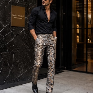 May include: A black long-sleeved button-down shirt with a collar and cuffs, paired with slim-fit trousers featuring a brown, black, and tan snakeskin print pattern. The outfit is completed with black leather boots and dark-tinted sunglasses.