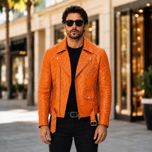 May include: A bright orange leather motorcycle jacket with a textured ostrich-skin pattern, featuring silver-tone metal zippers, a notched lapel, a waist belt with a buckle, and a small flap pocket on the front, worn over a plain black shirt.