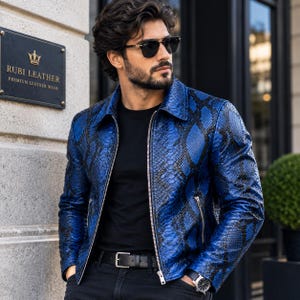 May include: A vibrant blue and black snakeskin-patterned leather jacket with a classic collar, long sleeves, and a silver-toned front zip closure. The jacket features two side pockets with silver zips and is worn over a plain black t-shirt.