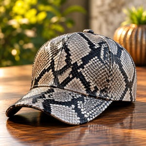 May include: A baseball cap featuring a detailed snakeskin pattern in shades of black, white, and gray. The cap has a structured six-panel crown, a curved brim, and a small button at the top center, showcasing a consistent reptilian scale texture.