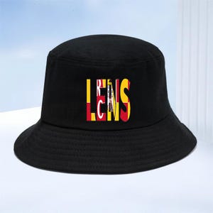 Può includere: Un cappello a secchiello nero a tinta unita con la parola LENS stampata in grandi lettere maiuscole sulla parte anteriore. Le lettere sono riempite con un motivo rosso, giallo e nero che ricorda il design della bandiera dello stato del Maryland.