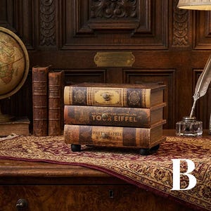 May include: A three-drawer storage chest designed to resemble a stack of vintage books. The drawers feature brown and tan spines with text including Tour Eiffel and Phytographia, each equipped with a small round knob and four black feet.