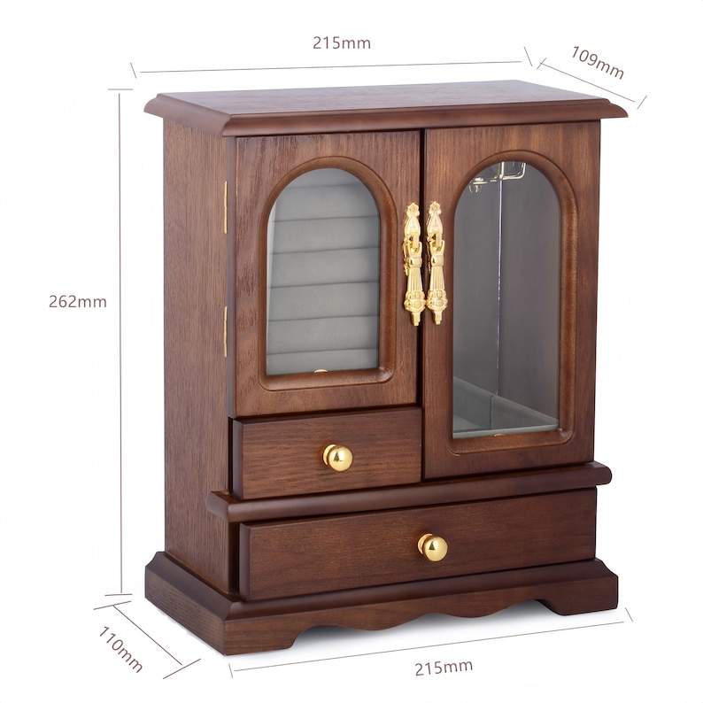 Op de afbeelding: Een donkerbruine houten sieradenkast met twee lades, goudkleurige knoppen en twee glazen deuren. De kast is 215 mm breed, 109 mm diep en 262 mm hoog. Het interieur is voorzien van een grijze fluwelen voering en een rek voor accessoires.