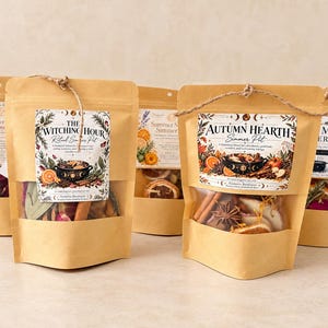 May include: Five brown paper pouches with clear windows containing dried botanical simmer pot ingredients. Each pouch features a decorative label with text including The Witching Hour, Autumn Hearth, and Summer Simmer, tied with twine.