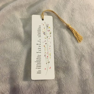 Peut inclure: Un marque-page blanc avec un motif floral et un gland doré. Le marque-page présente une citation en anglais et en hébreu : « Si vous croyez qu'il est possible de causer des dommages, croyez qu'il est possible de réparer. » - Rebbe Nachman de Breslov.