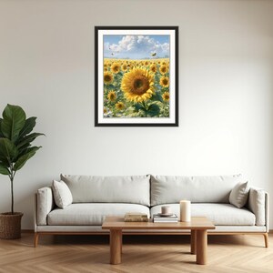 Pu&ograve; includere: Una stampa incorniciata di un campo di girasoli sotto un cielo blu con nuvole bianche. I girasoli hanno petali gialli e centri marrone scuro. La stampa &egrave; esposta sopra un divano grigio in un soggiorno.
