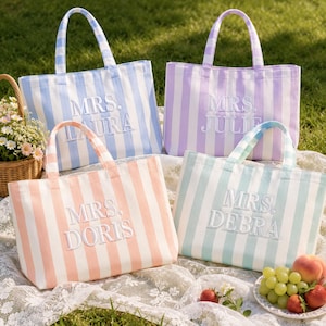 May include: Four rectangular canvas tote bags with vertical stripes in light blue, lavender, peach, and mint green. Each bag features two top handles and white embroidered text reading MRS. LAURA, MRS. JULIE, MRS. DORIS, and MRS. DEBRA.