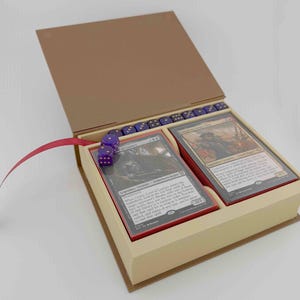 Könnte beinhalten: Eine beige Kartenspielbox in Buchform mit braunem Deckel und rotem Band. Im Inneren befinden sich zwei Kartenstapel und mehrere lila Würfel. Die Karten haben rote Ränder und schwarzen Text.