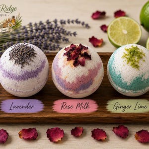 May include: Three spherical bath bombs on a wooden tray. The first is white with purple swirls and lavender buds. The second is white with pink and orange swirls topped with dried rose petals. The third is white with green swirls and lime zest.