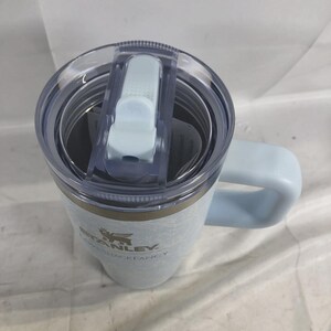 Puede incluir: Un vaso Stanley LoveShackFancy de color azul claro con tapa de pl&aacute;stico transparente y asa azul claro. El vaso presenta una superficie texturizada y el logotipo de Stanley LoveShackFancy impreso en oscuro en el lateral. La tapa tiene un mecanismo deslizante.