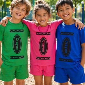 May include: Three short-sleeved t-shirts and matching shorts sets in green, pink, and blue. Each shirt features a black graphic print of a crayon wrapper design with a central oval containing the word Crayon and wavy lines above and below.