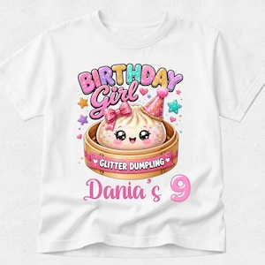 May include: A white t-shirt featuring a graphic of a smiling dumpling in a bamboo steamer. The dumpling wears a pink party hat and bow. Text reads "BIRTHDAY Girl", "GLITTER DUMPLING", and "Dania's 9". Colorful stars and sparkles surround the central design.