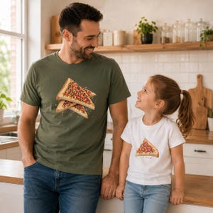 May include: An olive green t-shirt featuring a graphic of two slices of toast topped with colorful sprinkles, and a white t-shirt featuring a graphic of a single slice of toast topped with colorful sprinkles, both paired with blue denim jeans.