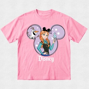 Puede incluir: Una camiseta rosa claro de manga corta con un gr&aacute;fico de Anna de Frozen y Olaf dentro de una silueta de orejas de Mickey Mouse. Anna lleva orejas negras y sostiene un helado azul. La palabra Disney est&aacute; impresa en blanco bajo el gr&aacute;fico.