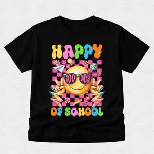 以下が含まれることがあります： HAPPY 100 DAYS OF SCHOOLという文字がプリントされた黒の半袖Tシャツ。サングラスをかけた黄色いスマイリーフェイス、ピンクと黒のチェック柄の背景、花、鉛筆、紙飛行機が描かれたグラフィックデザインが特徴です。