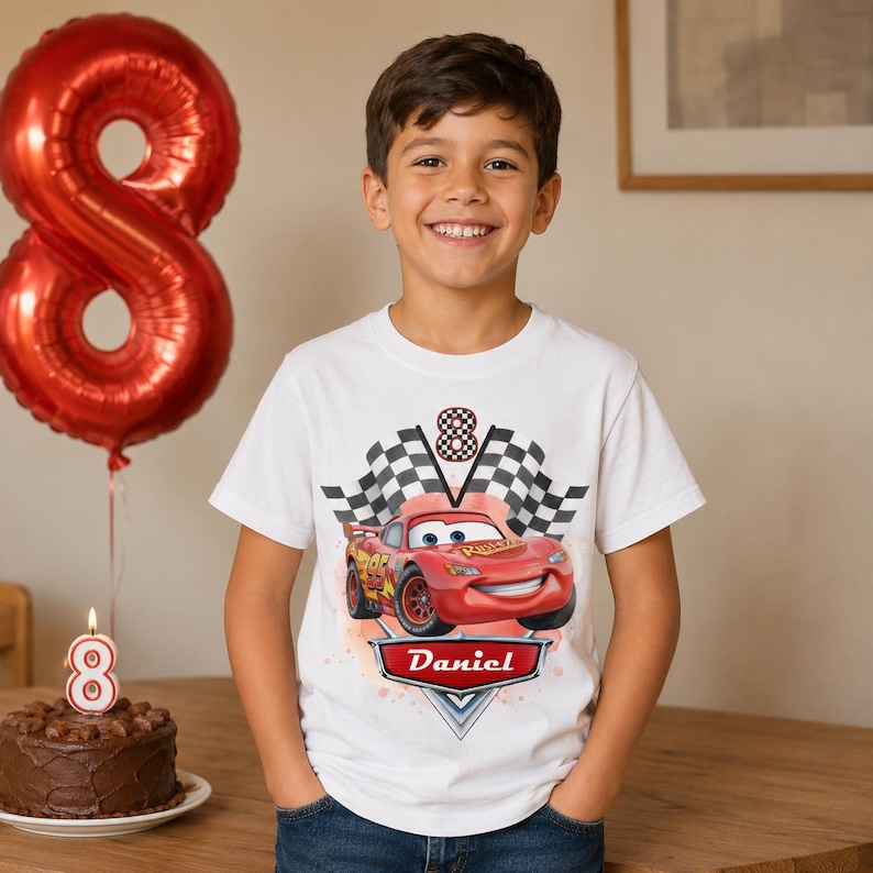 Peut inclure: Un t-shirt blanc avec une voiture de course rouge de dessin anim&eacute; et le nom "Daniel" sur une banni&egrave;re. Le t-shirt a un motif de drapeau &agrave; damier et le chiffre "8". Un ballon rouge en forme de 8 et un g&acirc;teau au chocolat avec une bougie en forme de 8 sont &eacute;galement visibles.