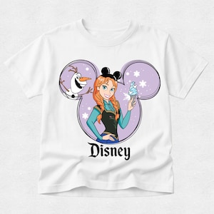 Puede incluir: Una camiseta blanca de manga corta con un gr&aacute;fico de Anna y Olaf dentro de una silueta de orejas de Mickey Mouse moradas. Anna tiene el pelo trenzado, lleva orejas negras y sostiene un helado azul. La palabra Disney aparece impresa en negro.