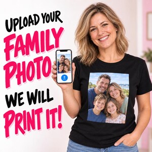 May include: A black t-shirt featuring a custom printed square photograph of a family of four. The image includes text that reads UPLOAD YOUR FAMILY PHOTO WE WILL PRINT IT in bold black and pink lettering next to a smartphone displaying the same photo.