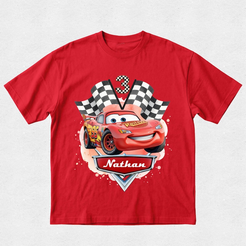 Peut inclure: T-shirt rouge avec un dessin de Flash McQueen du film Cars. Le motif comprend un drapeau &agrave; damier, le chiffre 3 et le nom "Nathan". La voiture est rouge avec des d&eacute;tails jaunes.