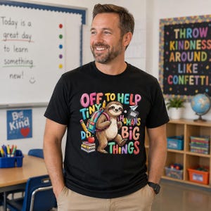Puede incluir: Una camiseta negra de manga corta con un gráfico colorido de un perezoso con mochila, rodeado de material escolar y el texto "OFF TO HELP TINY HUMANS DO BIG THINGS" en letras vibrantes y multicolores con estilo de burbuja.