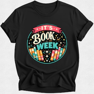 May include: A black short-sleeved t-shirt featuring a circular graphic with the text IT'S BOOK WEEK in white and blue. The design includes a row of colourful books at the bottom and small star accents against a dark background, centred on the chest.