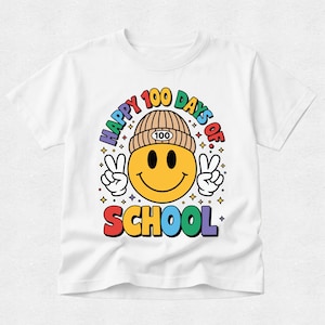 May include: A white t-shirt featuring a graphic of a yellow smiley face wearing a tan beanie with the number 100 on it. The smiley face is making peace signs with both hands. The text reads HAPPY 100 DAYS OF SCHOOL in colourful letters.
