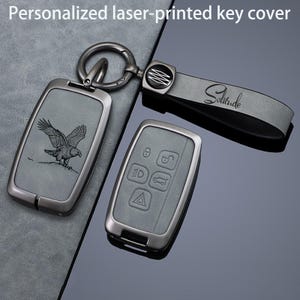 May include: A personalized laser-printed key cover set featuring a gray rectangular fob with an eagle engraving, a matching key fob case with five embossed buttons, and a gray leather strap with the word Solitude printed in black script.