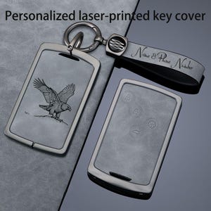 May include: A grey personalised laser-printed key cover set with a metal ring and leather strap. One cover features an eagle engraving, while the other shows car key button icons. The strap displays the text Name & Phone Number.