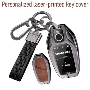 Puede incluir: Una funda de llave inteligente de metal gris oscuro con una pantalla digital que muestra el texto SMART KEY y la hora 17:29. Incluye una correa de cuero negro con un clip de metal y una pieza de cubierta secundaria con el nombre Rickroll grabado.