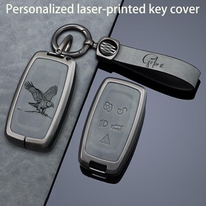 May include: A dark gray metal key cover set featuring a laser-engraved eagle on one piece and five functional vehicle control icons on the other. The set includes a matching gray leather strap with the text Go for it and a metal key ring.