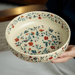 Peut inclure: Un bol rond en céramique avec une base de couleur crème présentant une texture mouchetée et un motif décoratif de fleurs orange et de feuilles bleu sarcelle foncé. Le motif floral est imprimé sur les surfaces intérieure et extérieure.