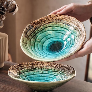 Pode incluir: Dois recipientes de cerâmica com um interior vibrante em tons de turquesa e azul-petróleo, com uma borda castanha escura salpicada. Os recipientes têm uma superfície texturizada e ondulada com acabamento brilhante e padrões circulares.