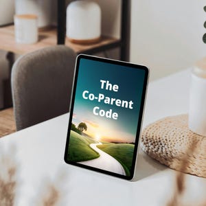 Puede incluir: Una tableta que muestra el texto "The Co-Parent Code" contra un fondo escénico de un camino sinuoso a través de colinas verdes al atardecer. La tableta está sobre una superficie blanca, con una estera tejida y elementos decorativos en el fondo.