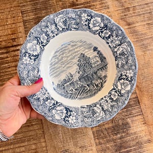 Puede incluir: Una taza de cerámica blanca con asa negra y el texto "But First, Coffee" en negrita negra. La taza se encuentra sobre un fondo neutro, resaltando su diseño sencillo.