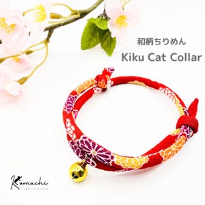 May include: Red Kiku cat collar with floral pattern and a gold bell. The collar features the text "Kiku Cat Collar" and Japanese text. The collar is made of a patterned fabric with orange, purple, and yellow flowers.