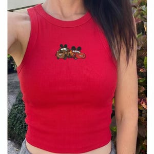 May include: A red ribbed tank top featuring a graphic of two cartoon cars. The sleeveless top has a crew neck and is made of a soft, stretchy material. The graphic is located on the upper chest area.
