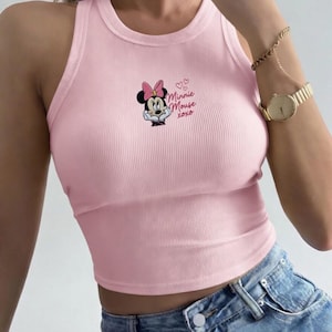 May include: A light pink ribbed crop top featuring a Minnie Mouse graphic with a pink bow and the text "Minnie Mouse xoxo". The top has a round neckline and a sleeveless design.